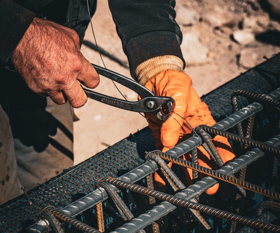 A worker in orange gloves tying reinforcing bar into a cage with pliers